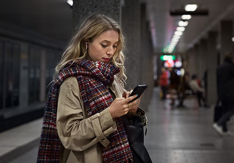 Høstkledd kvinne på t-banestasjonen ser på mobilen sin.