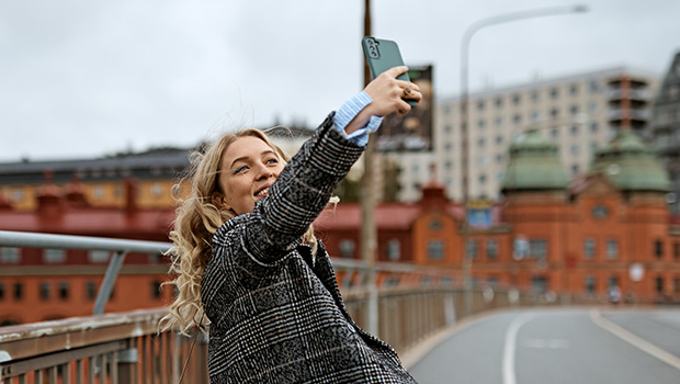 Høstkledt, blid ung kvinne står på en bro og tar selfie.