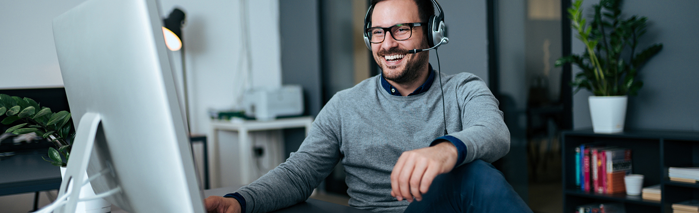 Mann på hjemmekontor med headset deltar i digitalt møte. 