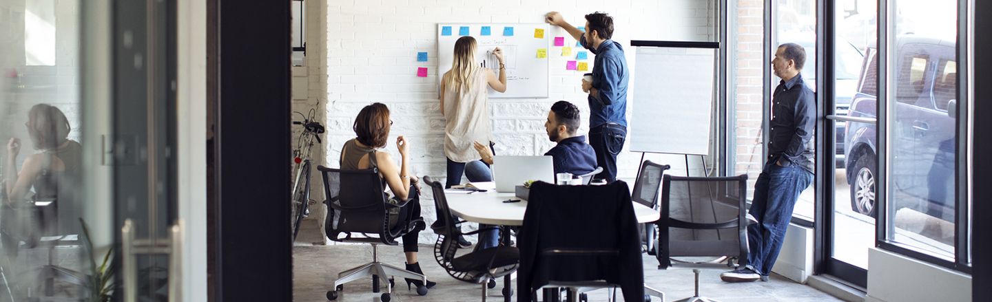 5 personer i et arbeidsrom med post-it-lapper og tavle gjennomfører en designsprint. 