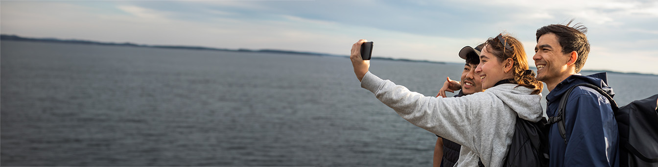 Ungdommer står ved sjøen og tar selfie i solen