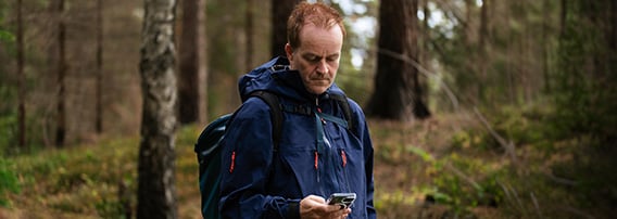 Mann med mobil og turklær i skogen